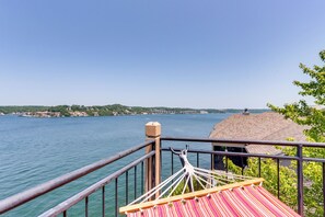 A hammock on a balcony overlooking a lake with buildings in the distance.