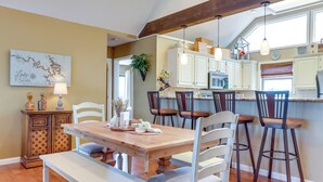 A dining area with a wooden table and chairs, a bench, and a kitchen in the background. - Pool Access + Views: Waterfront Lake Ozark Escape (Lake Ozark)