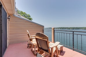 A wooden deck with Adirondack chairs and a table overlooking a body of water.