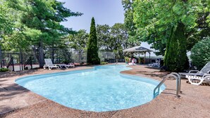A swimming pool with a clear blue water, surrounded by lounge chairs and a covered seating area. - Pool Access + Views: Waterfront Lake Ozark Escape (Lake Ozark)