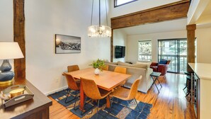 A spacious living area with a wooden dining table, comfortable seating, a large window, and a view of the outdoors.