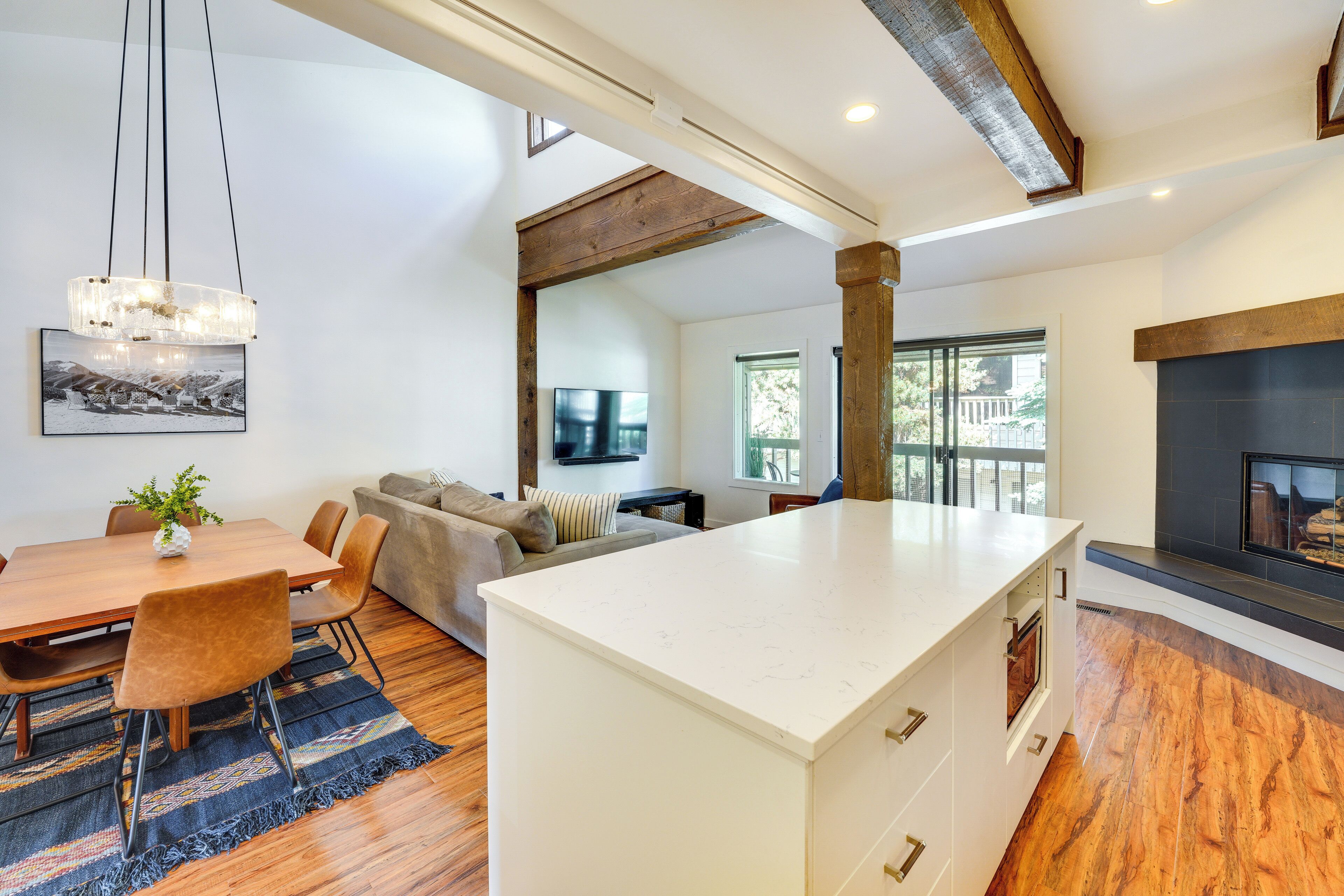 A modern kitchen with a central island, wooden flooring, and a large window providing natural light.