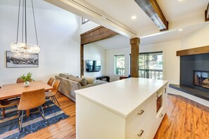 A modern kitchen with a central island, wooden flooring, and a large window providing natural light.