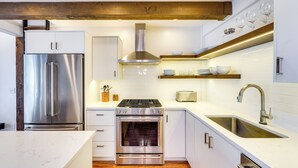 A modern kitchen with stainless steel appliances, white cabinetry, and a wooden ceiling.