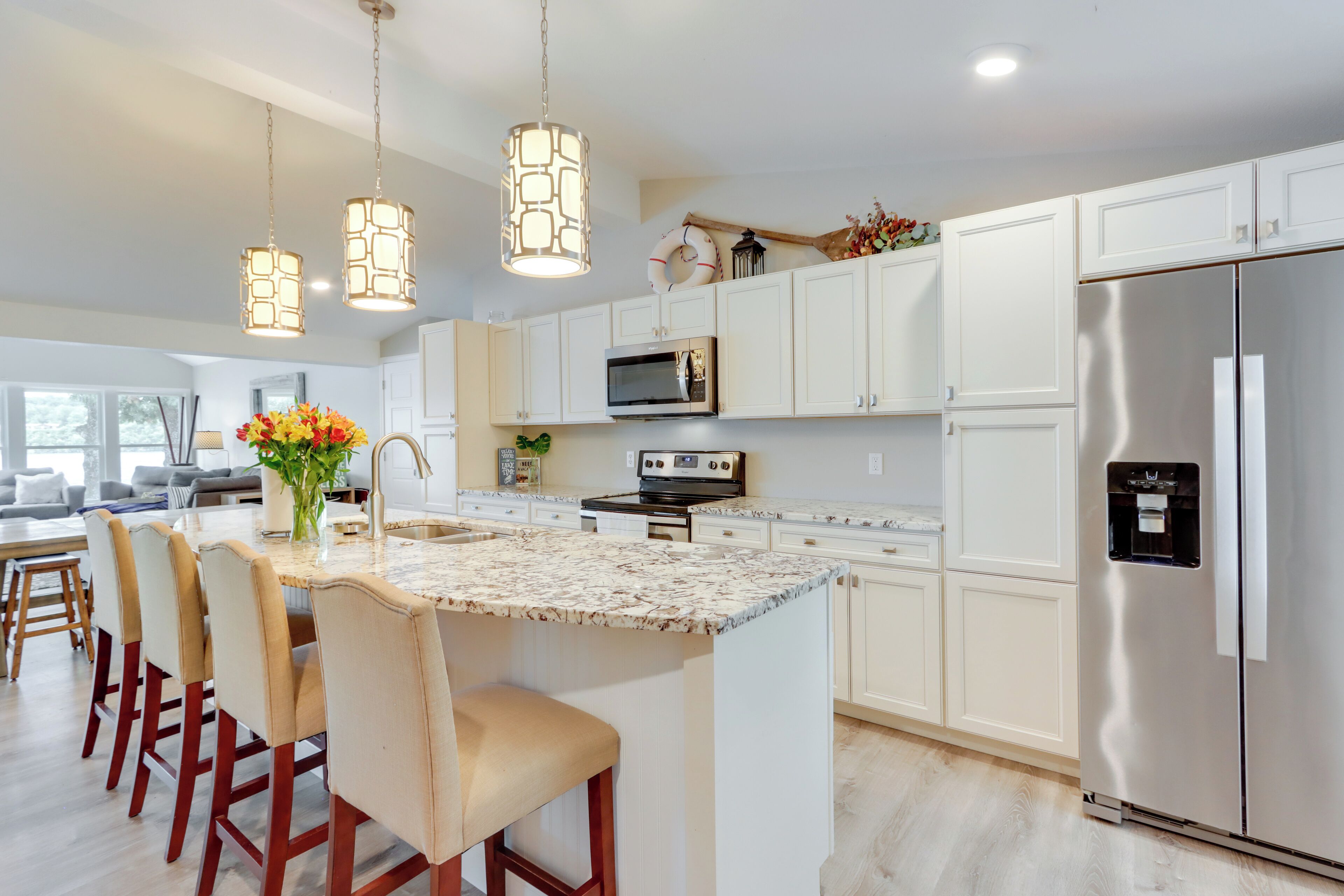 A modern kitchen with white cabinets, stainless steel appliances, a marble island, and pendant lighting.