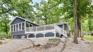 A two-story house with a balcony, surrounded by trees and a gravel driveway. - Dock & Sunset Views: Lakeside Ozark Retreat! (Lake Ozark)