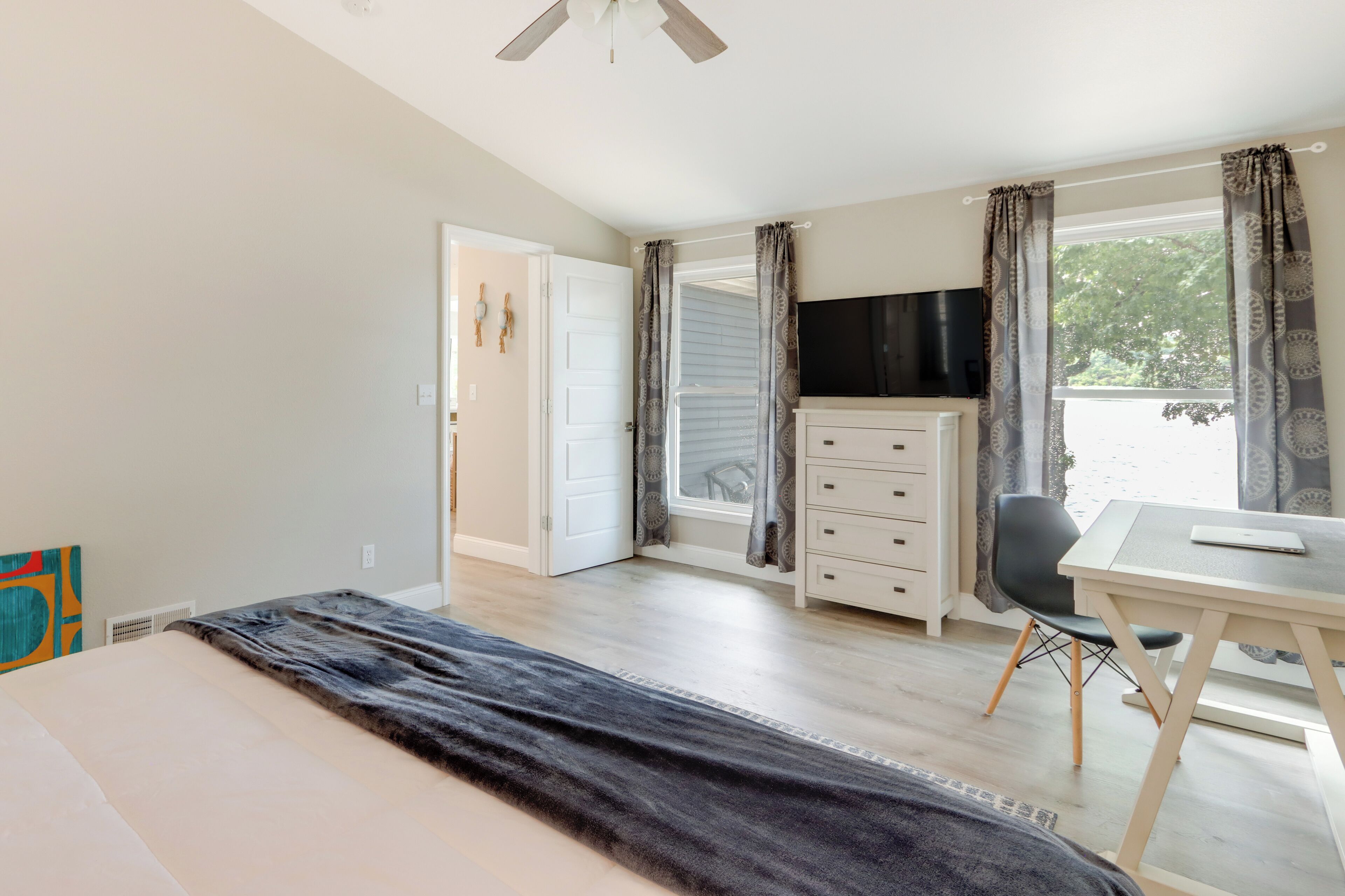 Een slaapkamer met een bed, een bureau, een stoel, een dressoir, een televisie en een raam met gordijnen.