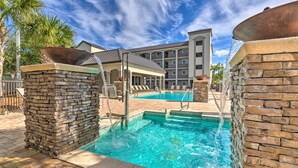A swimming pool with stone walls, a covered seating area, and a building in the background. - Miramar Beach Condo w/ Pool - Walk to Beach! (Miramar Beach)