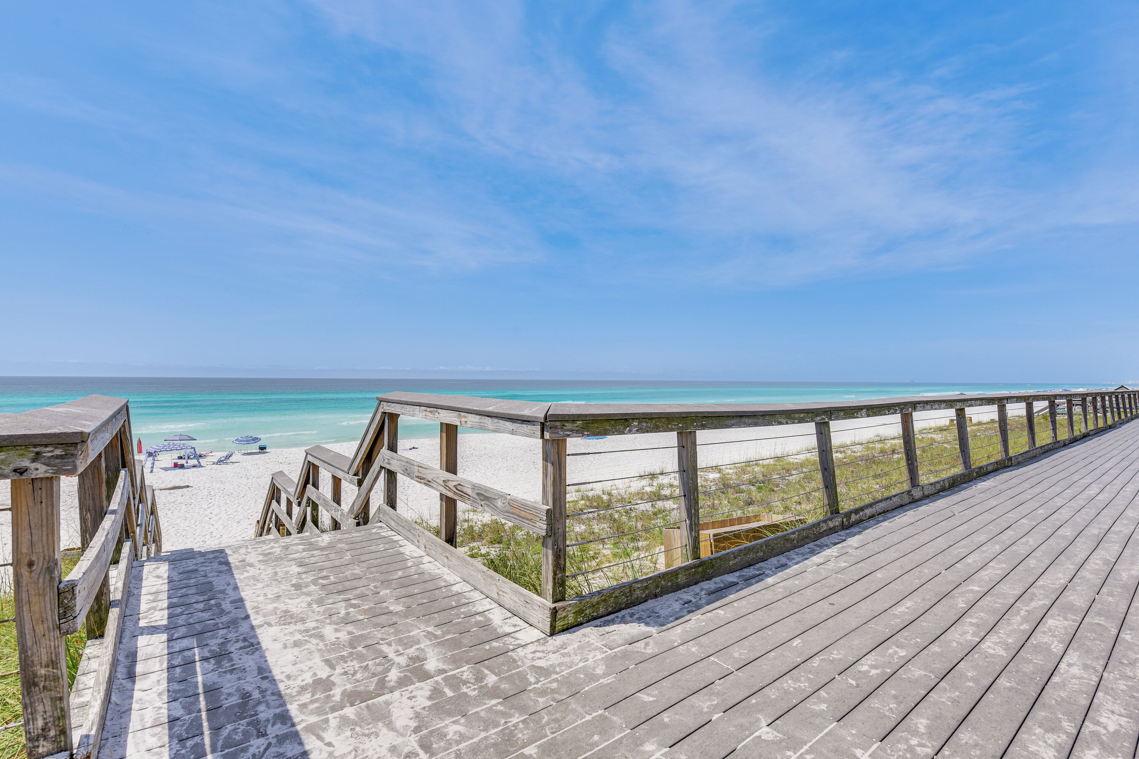 A wooden boardwalk leading to a beach with clear turquoise water and a clear sky.