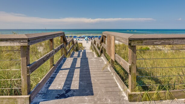 Een houten looppad naar een strand met parasols en mensen.