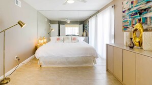 Ein Schlafzimmer mit Bett, Nachttischlampen, Deckenventilator, einem großen Spiegel und einem Wanddekor.