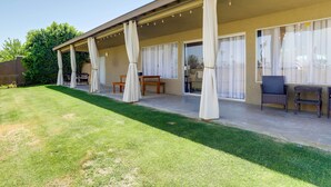 Ein überdachter Patio-Bereich mit Rasenfläche, Gartenmöbeln und Vorhängen.