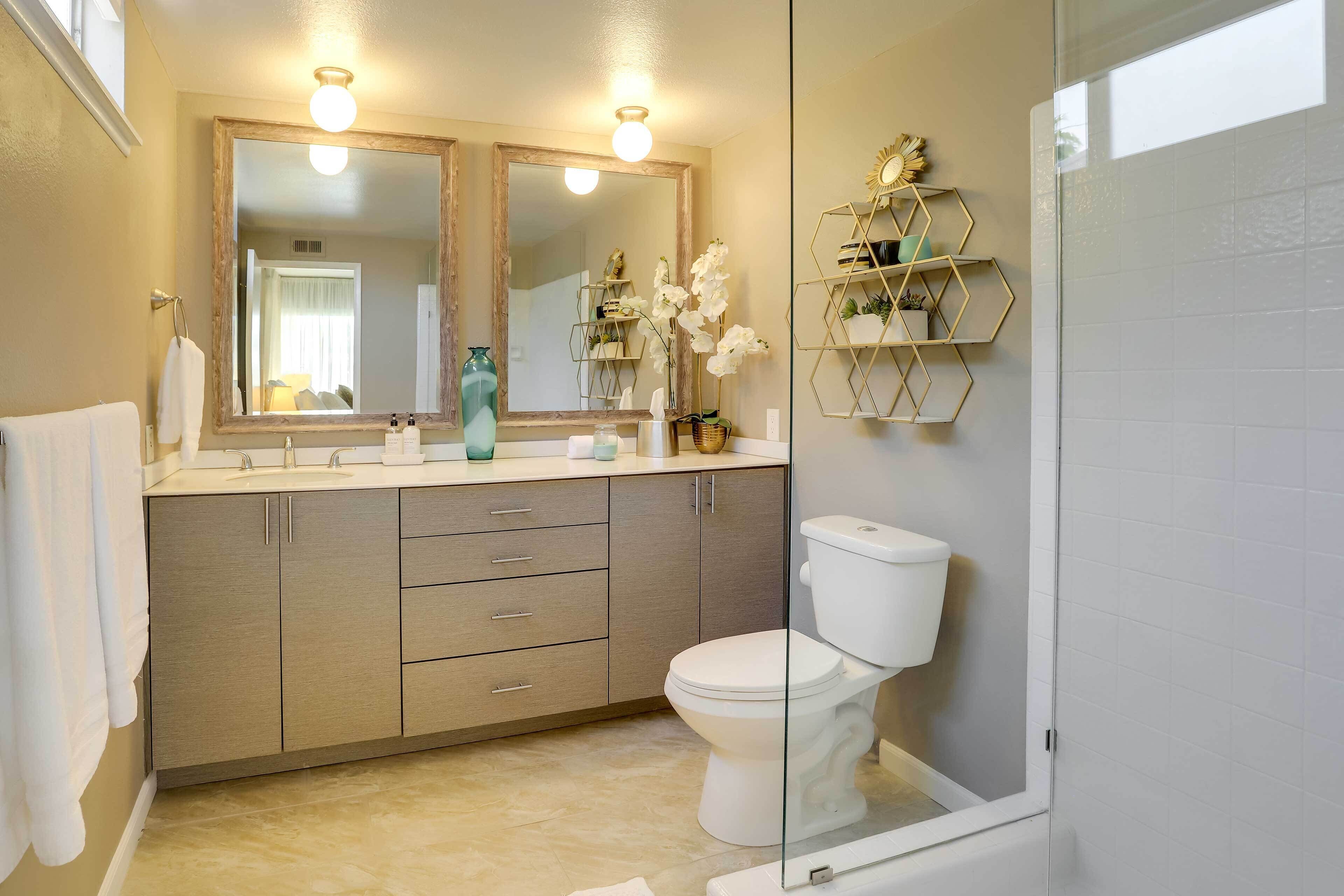 A modern bathroom with a beige vanity, double mirrors, a white toilet, and a glass shower enclosure.