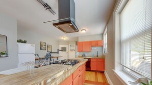 A modern kitchen with a central island, wooden flooring, and orange cabinetry. - Inviting St Louis Apartment - Great Location! (St. Louis)
