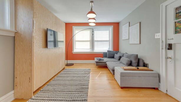 A modern living room with a grey sofa, a wooden cabinet, a flat-screen TV, and a patterned rug. - Inviting St Louis Apartment - Great Location! (St. Louis)