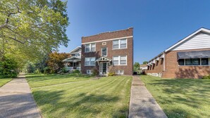 A two-story brick building with a front porch and a well-maintained lawn. - Inviting St Louis Apartment - Great Location! (St. Louis)