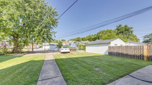 A residential backyard with a lawn, a wooden fence, and a white car parked in the driveway. - Inviting St Louis Apartment - Great Location! (St. Louis)