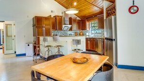 Une cuisine moderne avec des meubles en bois, un réfrigérateur en acier inoxydable et un coin repas comprenant une table en bois et des tabourets de bar.
