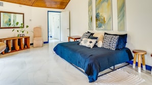 Une chambre avec un grand lit, une console en bois, une chaise et des tableaux abstraits accrochés au mur.