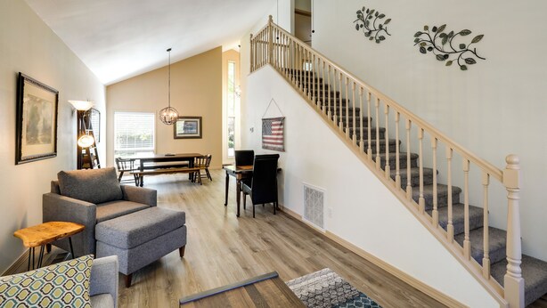 Ein geräumiges Wohnzimmer mit hoher Decke, einer Treppe mit Holzwerteln und einem Essbereich mit Tisch und Stühlen.