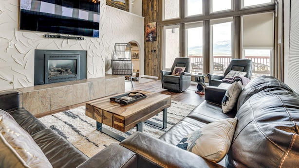 A modern living room with a fireplace, leather sofas, a coffee table, and a large window with a view. - Hot Tub Relaxation: Luxe Summit Gem w/ Mtn Views (Dillon)