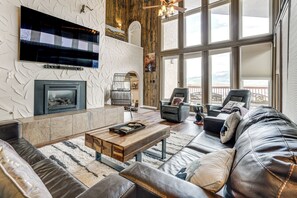 A modern living room with a fireplace, leather sofas, a coffee table, and a large window with a view. - Hot Tub Relaxation: Luxe Summit Gem w/ Mtn Views (Dillon)