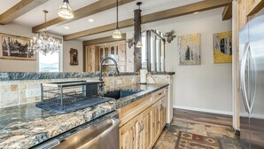 A kitchen with granite countertops, stainless steel appliances, wooden cabinets, a chandelier, and artwork on the walls. - Hot Tub Relaxation: Luxe Summit Gem w/ Mtn Views (Dillon)