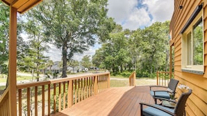 Una terraza de madera con dos sillas y una mesa, con vistas a una zona residencial con árboles y casas.