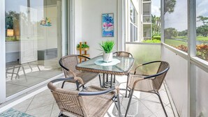Ein verglaster Balkon mit Korbmöbeln, einem Glastisch und einem Blumentopf.