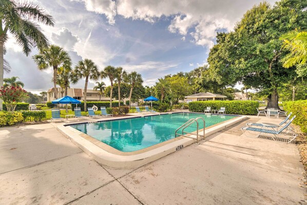 A swimming pool with lounge chairs and umbrellas, surrounded by palm trees and a cloudy sky. - Sunny Sarasota Oasis w/ Private Screened Lanai (Sarasota)