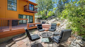 Un patio moderno al aire libre con un brasero, sillas de lounge y una terraza de madera.