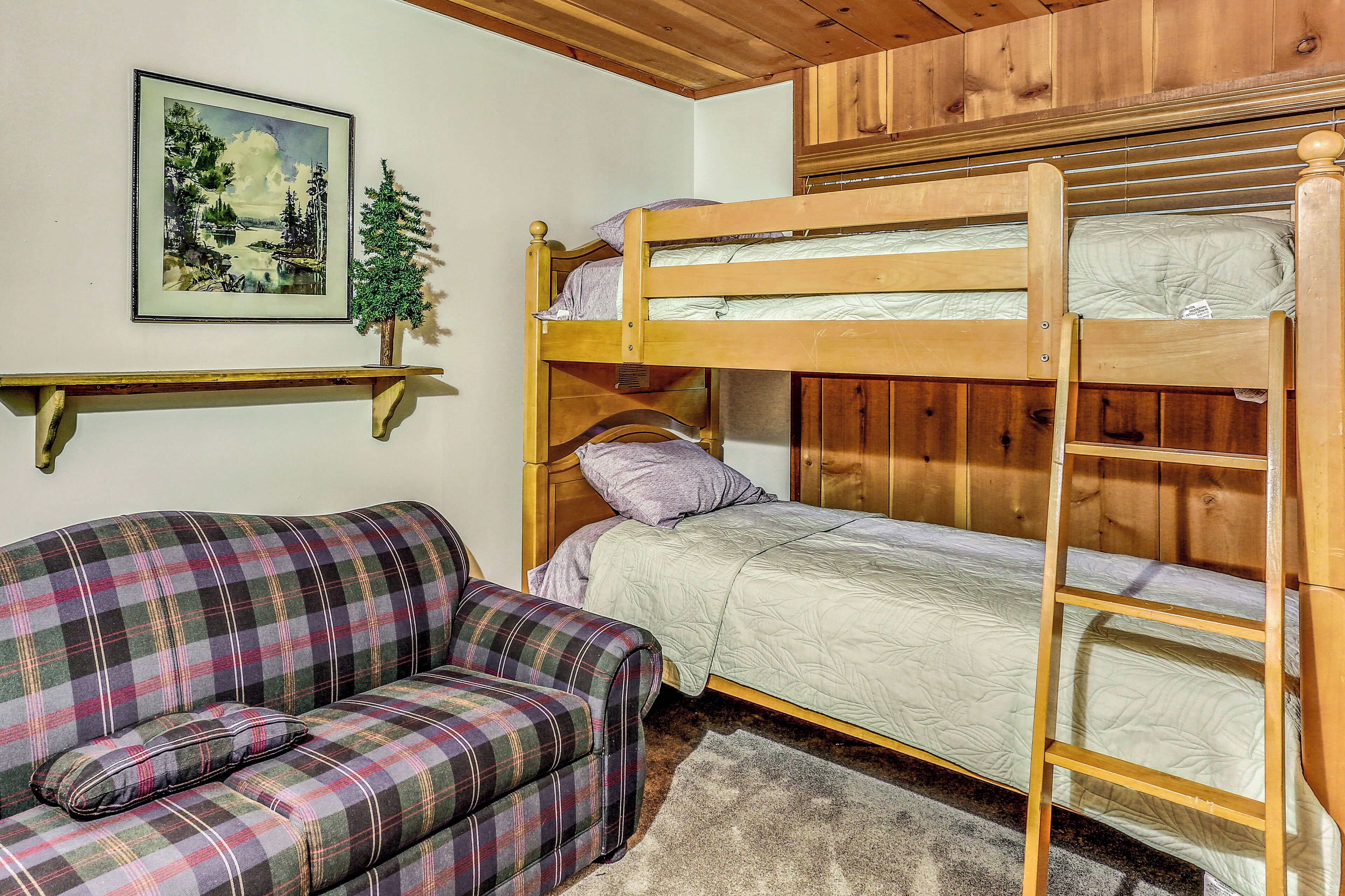 Una cama litera con escalera, un sofá a cuadros y un cuadro de un paisaje en la pared.