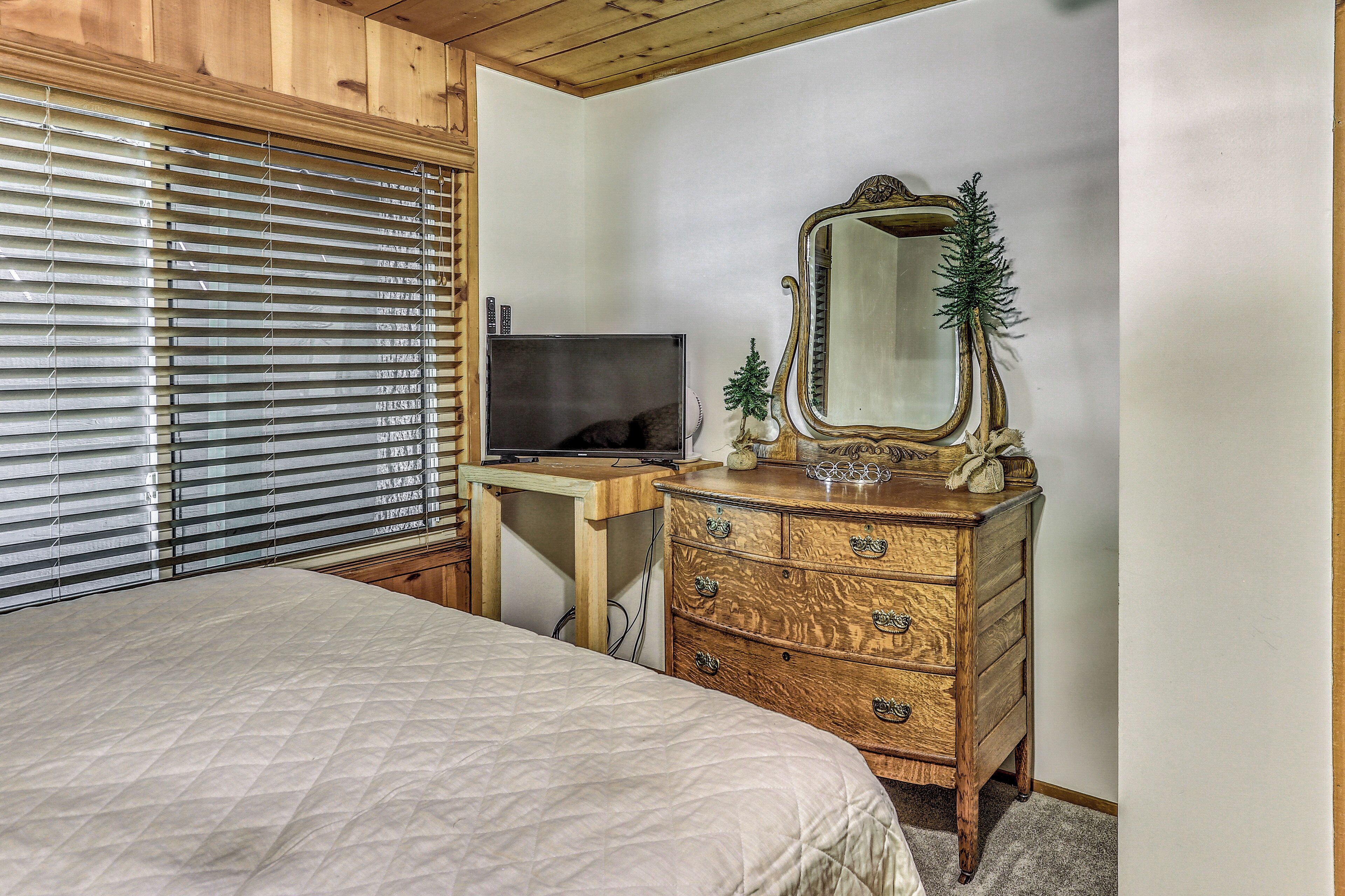 A bedroom with a bed, wooden dresser, mirror, and a TV on a desk.