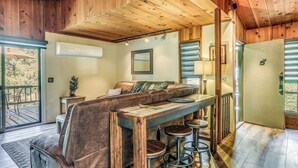 Interior acogedor de una cabaña con techo de madera, un sofá, una mesa de comedor con taburetes y una puerta corrediza.