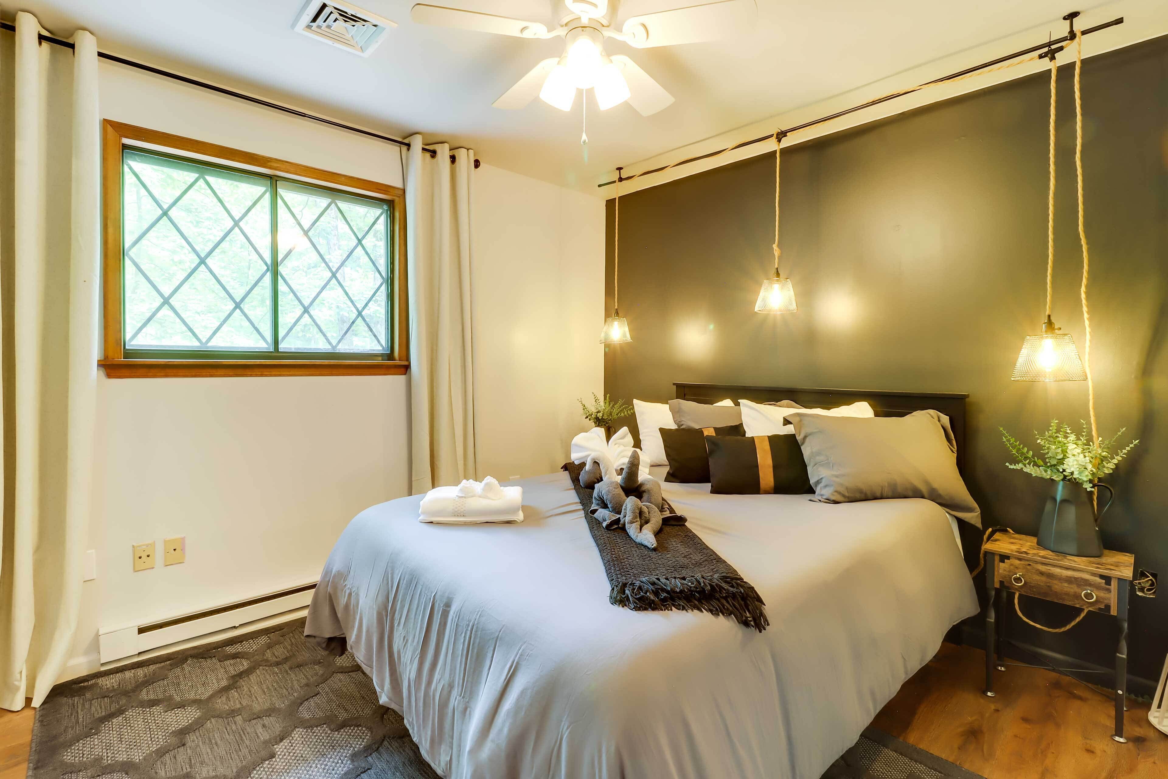 A neatly made bed with pillows and a blanket, a bedside table with a vase, and a window with curtains.