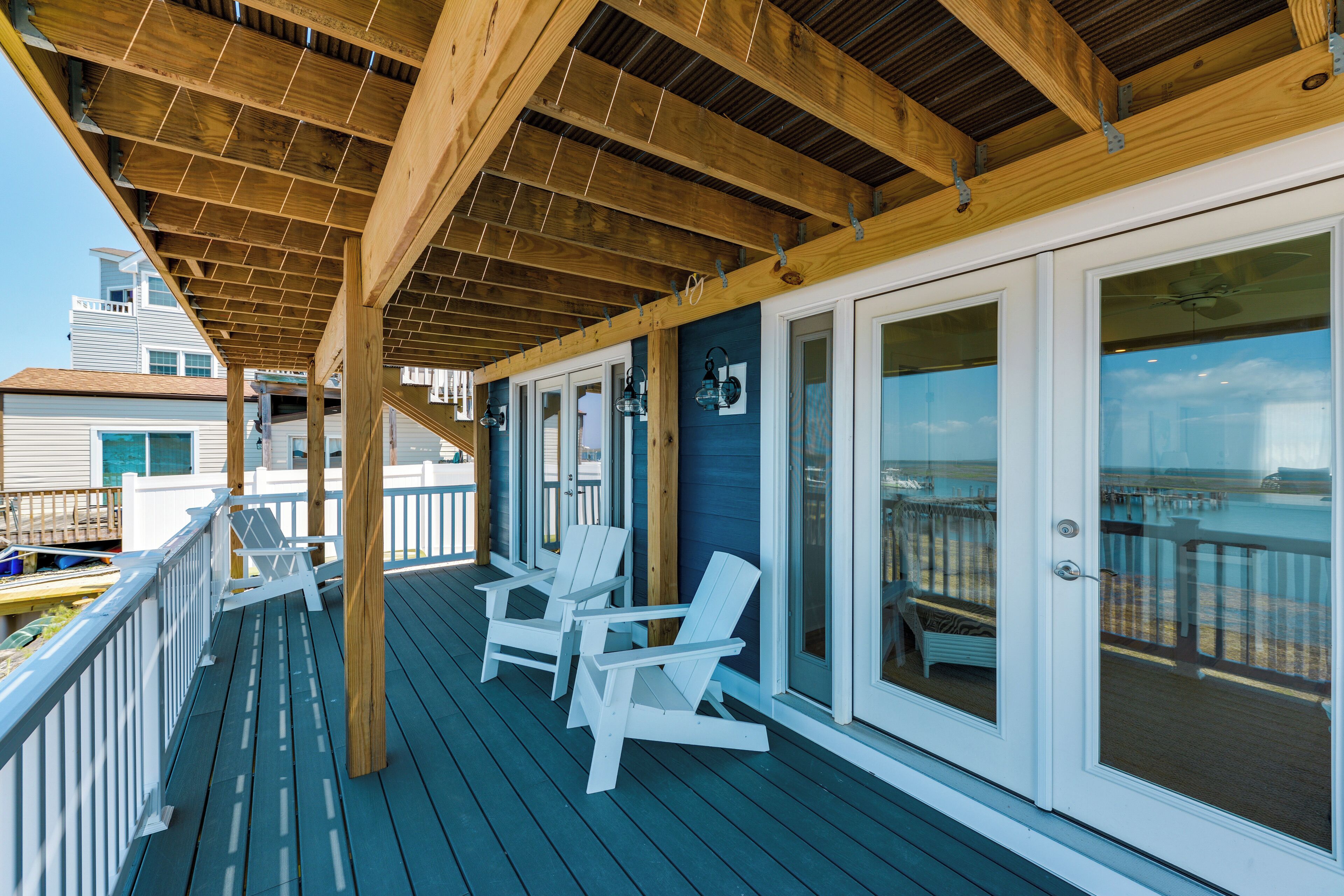 Um deck coberto com cadeiras Adirondack brancas, corrimão branco e vista para o oceano.