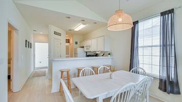 A modern kitchen with white cabinets, a central island, and a dining area with a white table and chairs.