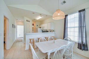Una cocina moderna con armarios blancos, una isla central y un comedor con mesa y sillas blancas.