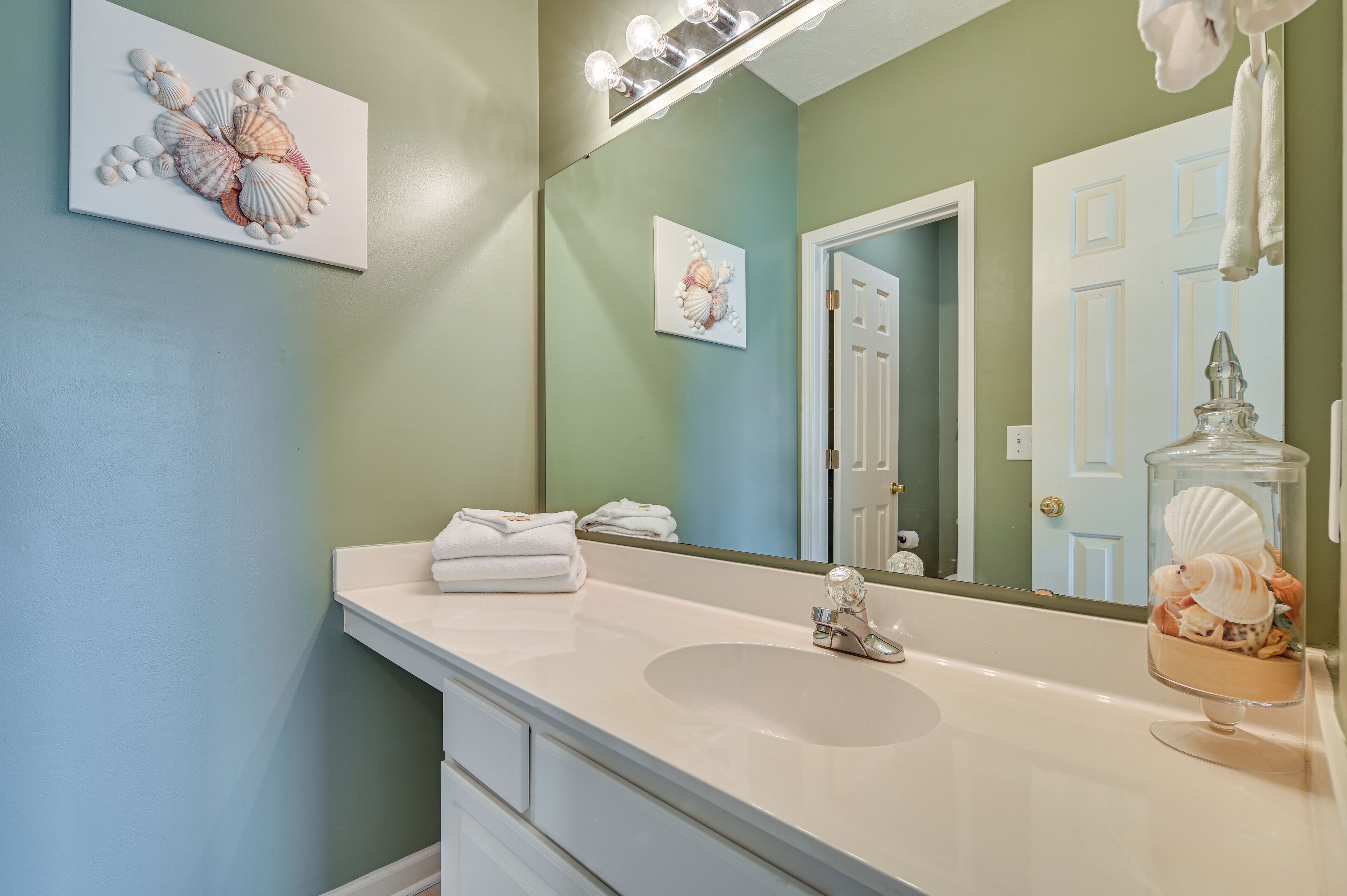A bathroom with a white sink, a large mirror, and a wall-mounted light fixture.