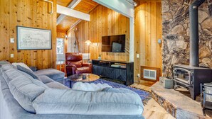 A cozy living room with a stone wall, wooden ceiling, a fireplace, a sofa, a TV, and a leather chair. - Mammoth Lakes Vacation Rental: 1 Mi to Ski Area! (Mammoth Lakes)