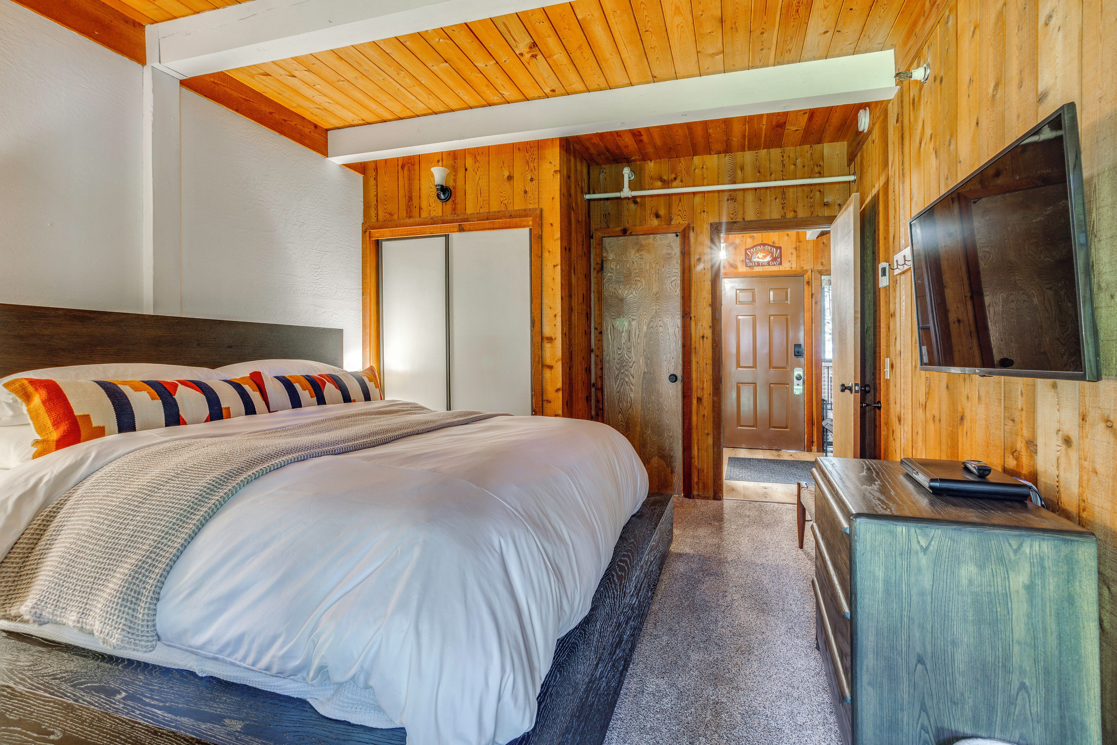 Un dormitorio con una cama grande, paredes de madera, un televisor y una puerta que da a otra habitación.
