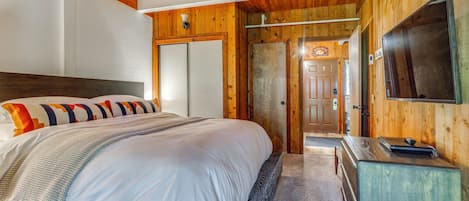 Un dormitorio con una cama grande, paredes de madera, un televisor y una puerta que da a otra habitación.