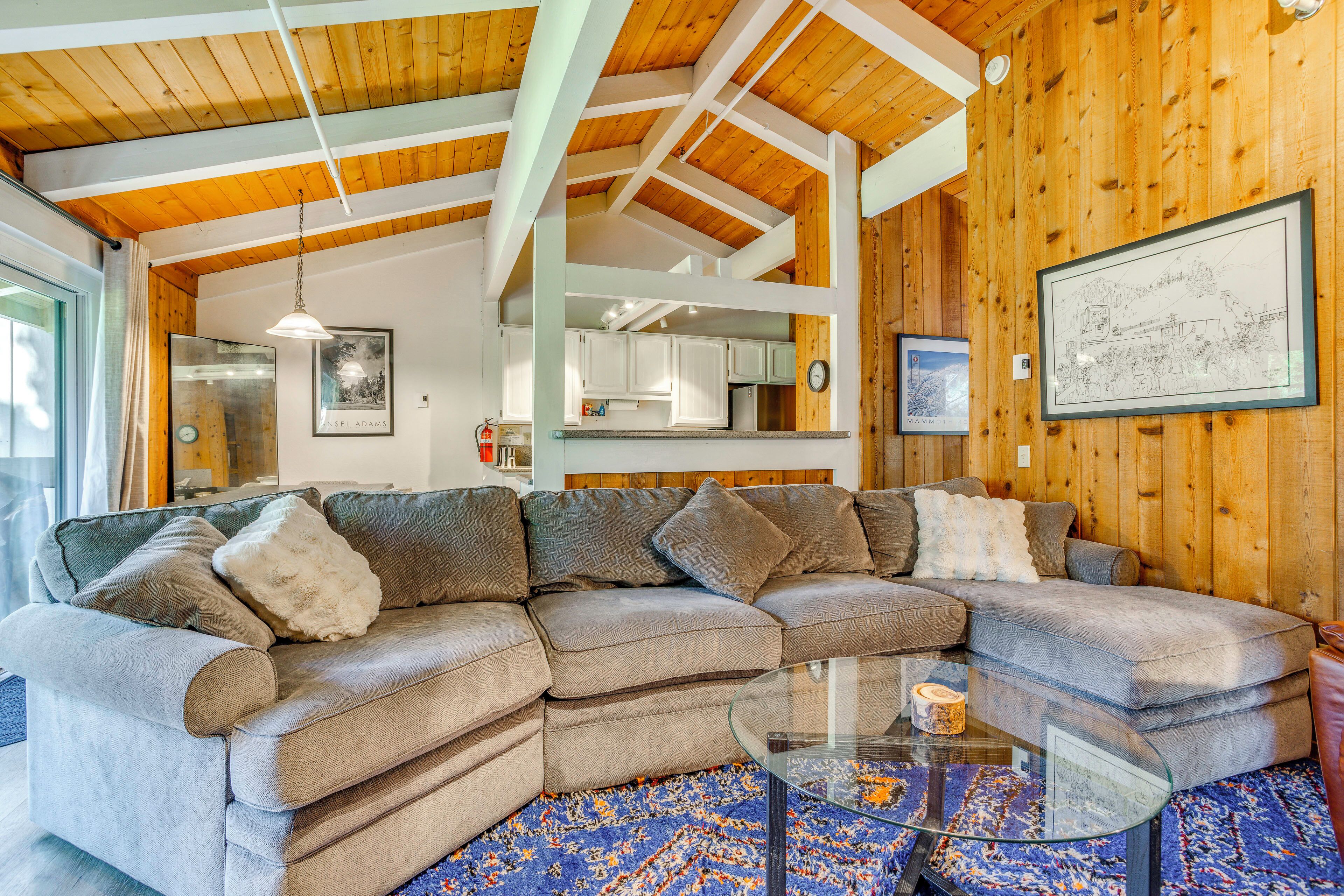 A modern living room with a sectional sofa, a glass coffee table, and wooden ceiling beams.