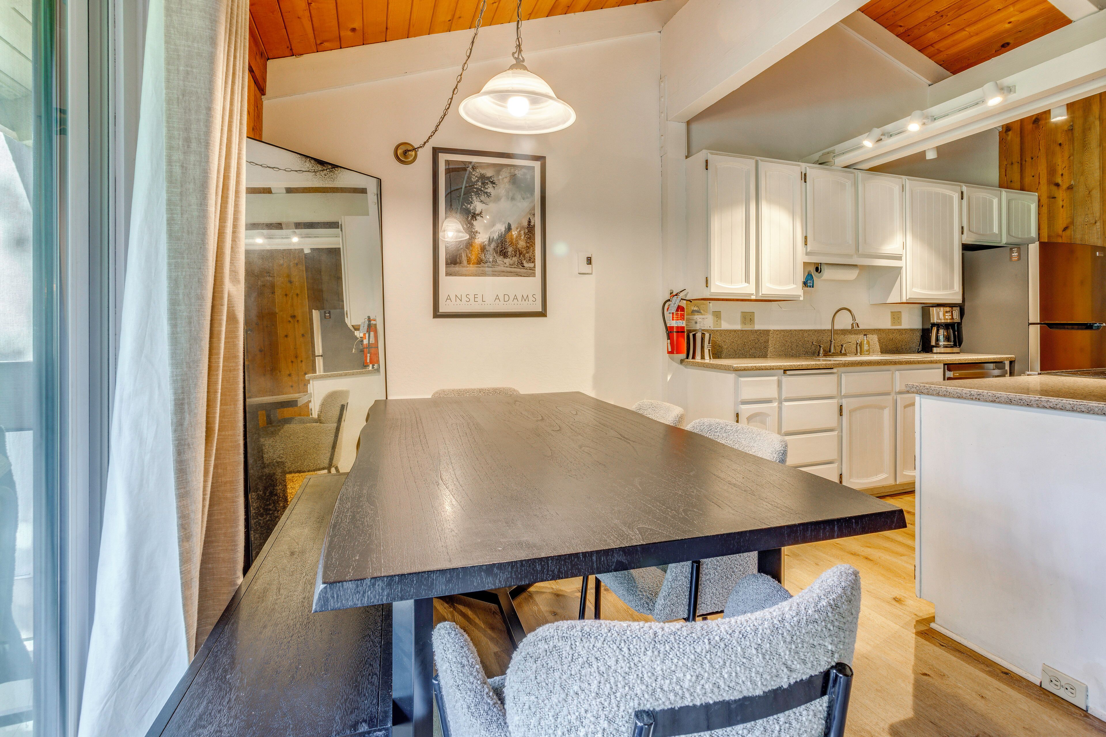 A modern kitchen with white cabinets, a wooden dining table, and a pendant light.