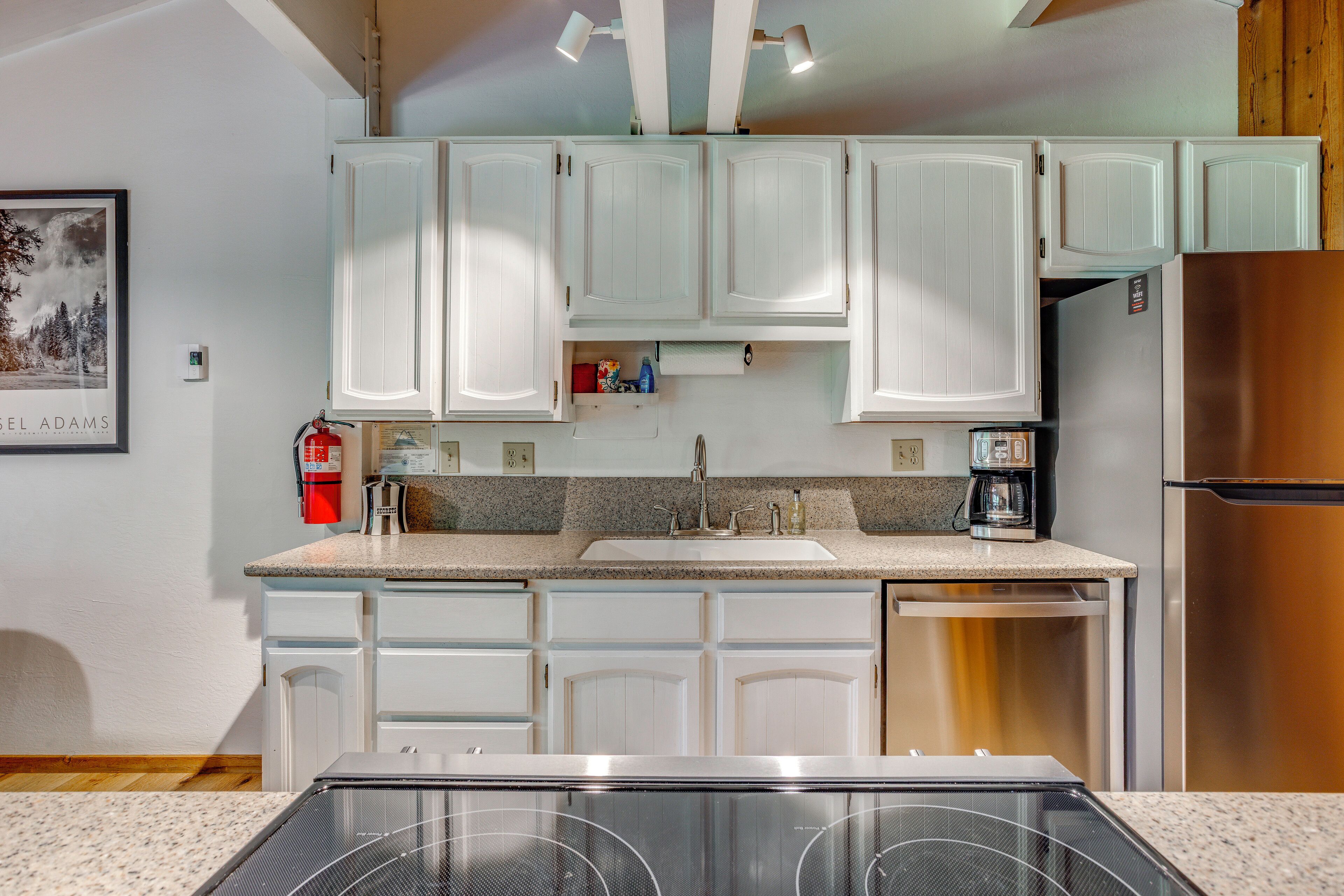 Una cocina con armarios blancos, un refrigerador de acero inoxidable, un horno empotrado y una cafetera.