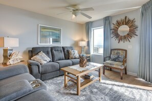 A living room with a grey sofa, a wooden coffee table, a patterned rug, and a decorative mirror on the wall. - North Myrtle Beach Oceanfront Condo w/ Pool Access (North Myrtle Beach)