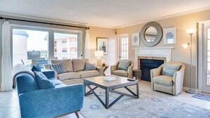 Un salon comprenant un canapé, des fauteuils, une table basse, une cheminée et une grande fenêtre avec des rideaux.