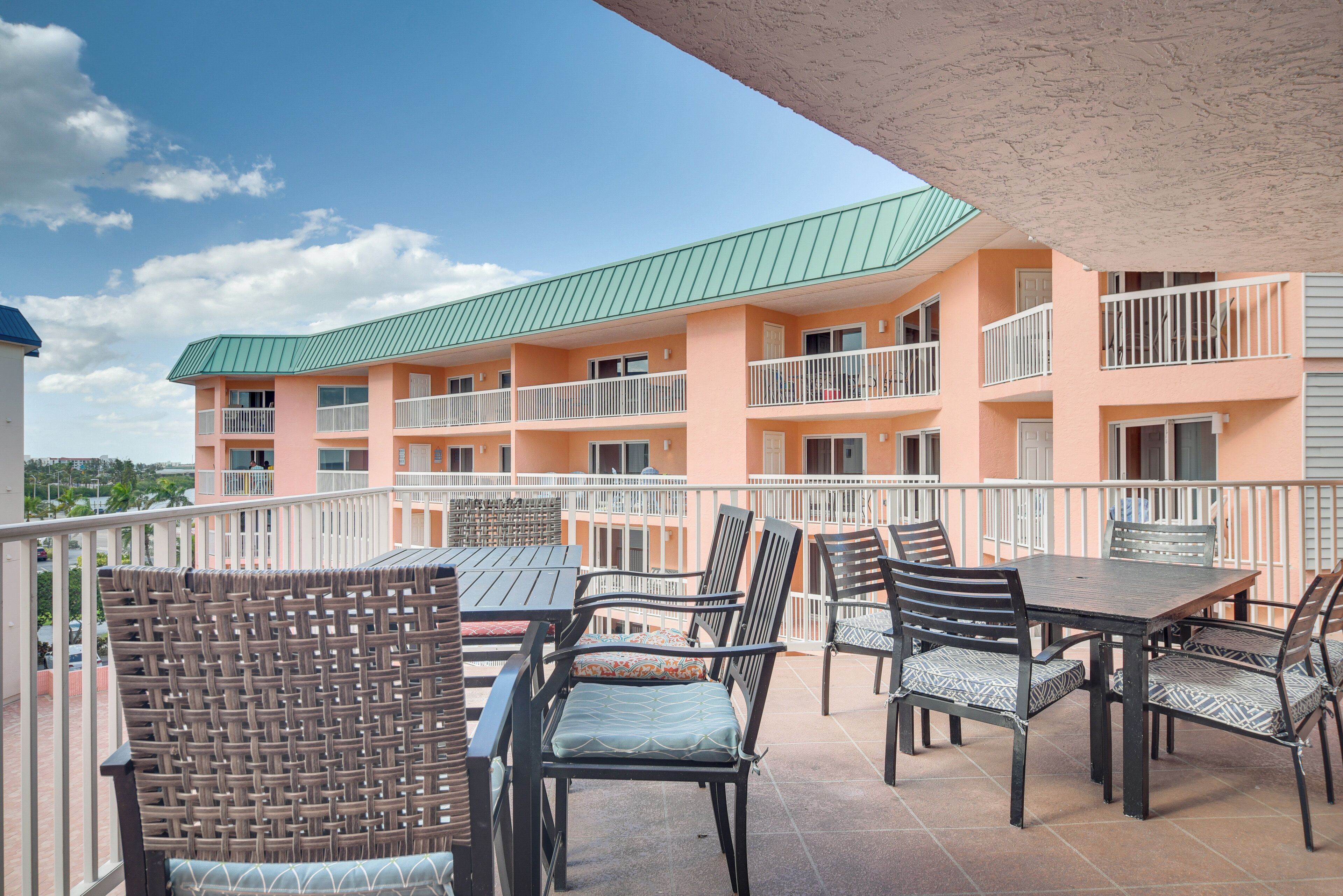 A balcony with wicker chairs and tables, overlooking a multi-story building with balconies.