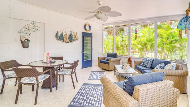 A bright, open living area with wicker furniture, a dining table, and a view of lush greenery outside. - Hot Tub & Gas Grill: Port Richey Retreat (Port Richey)