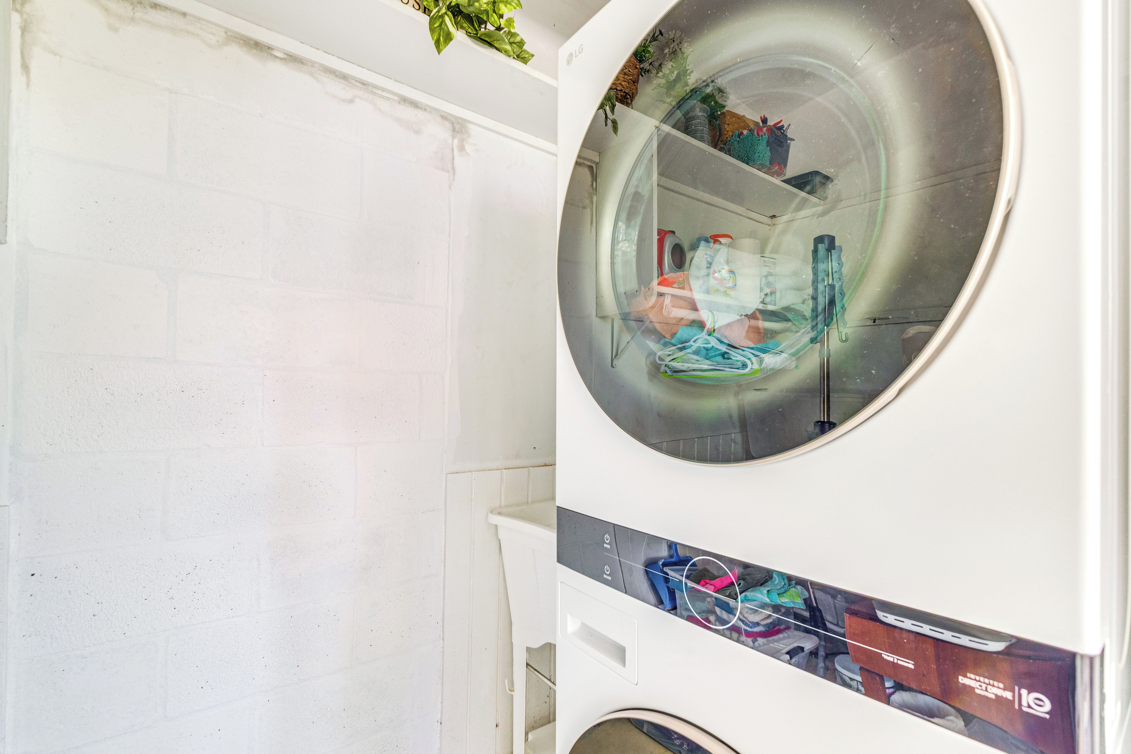 A laundry room with a large circular window, a white brick wall, and a shelf with various items.
